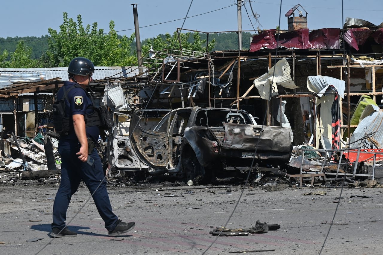 default-1205 A police officer is shown walking in an area filled with debris and damaged vehicles and structures.