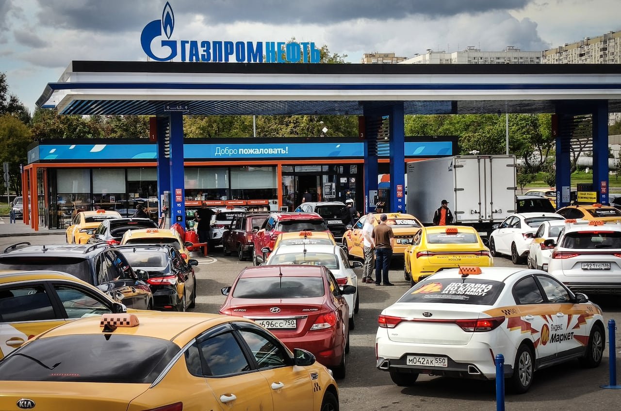 default-1206 Several vehicles, including many yellow cabs, are shown in a parking lot of a gas station.