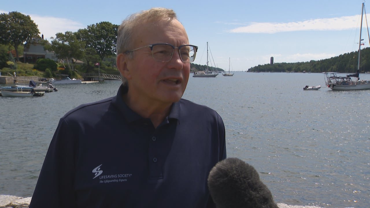 A man stands in front of the ocean and speaks to a CBC News Reporter.