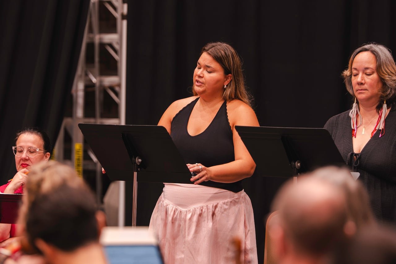 default-2170 A woman in a pink dress and black halter top singing with a music stand in front of her, accompanied by another woman behind a separate music stand.