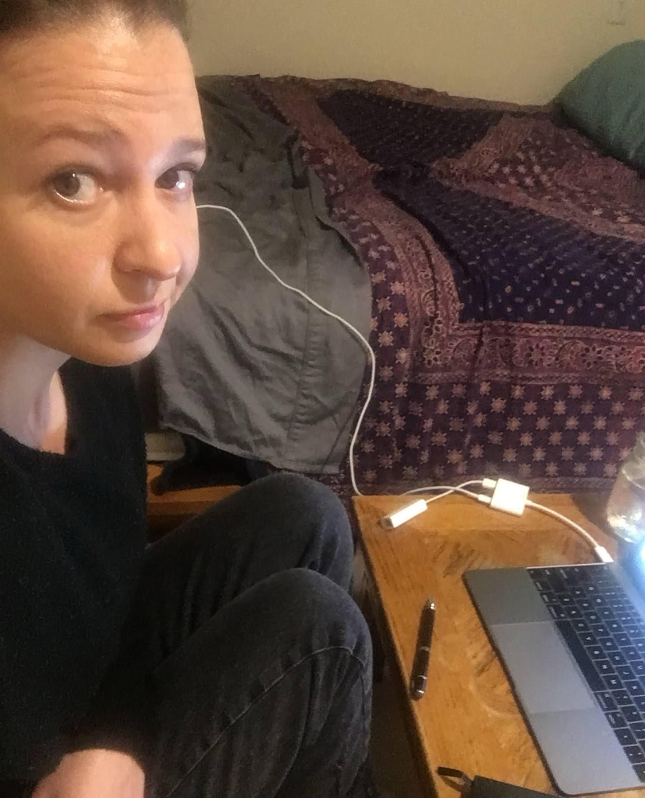 default-36 A woman poses for a selfie while sitting next to her laptop and bed.