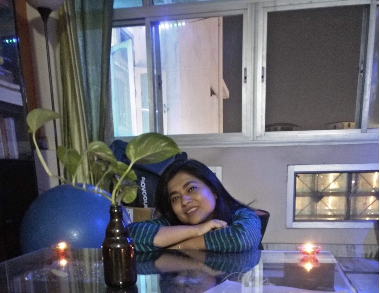 A woman sitting at a kitchen table with large windows in the background.