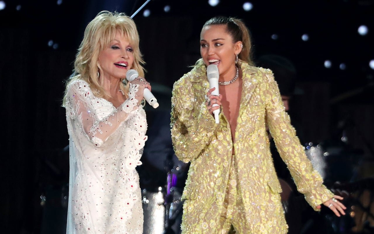 default-288 An elderly woman in a shimmering white ensemble performs on stage with a younger woman in a gleaming gold outfit.