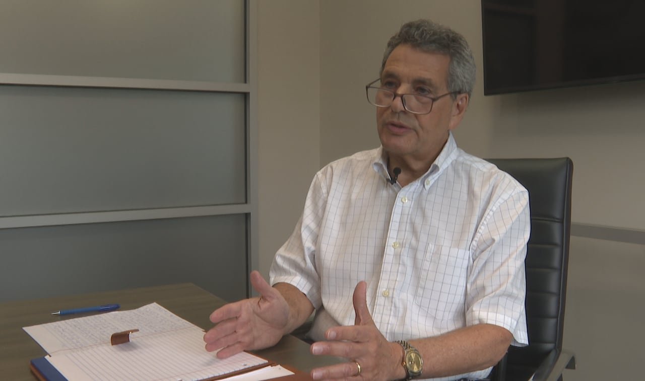 A middle aged man with glasses speaks while seated at a board room table
